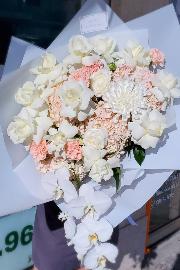 A sophisticated floral arrangement titled "Elegance in Bloom," featuring a harmonious blend of white roses, orchids, and hydrangeas, exuding timeless beauty and grace.