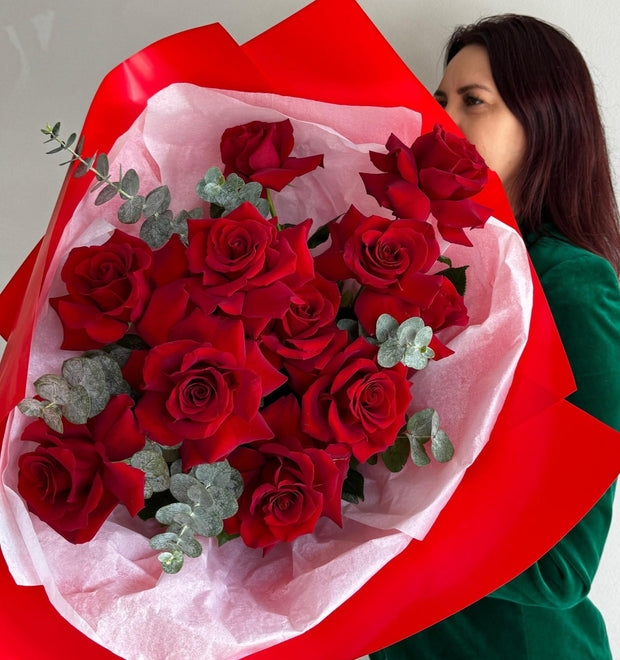 Striking arrangement of reflexed red roses with elegantly curled petals, paired with fresh eucalyptus sprigs, creating a bold and sophisticated floral display.
