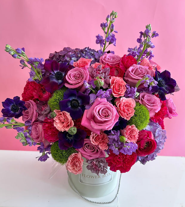 A luxurious flower box filled with pink and purple blooms, including elegant roses, delicate anemones, and ruffled carnations, perfect for a romantic gesture or a gift for someone who adores soft, feminine hues.