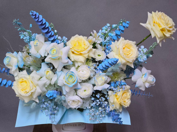 A delicate floral arrangement featuring white roses, ranunculus, stock, baby's breath, and eucalyptus with soft blue accents, symbolizing purity and new beginnings, perfect for celebrating the arrival of a baby boy.