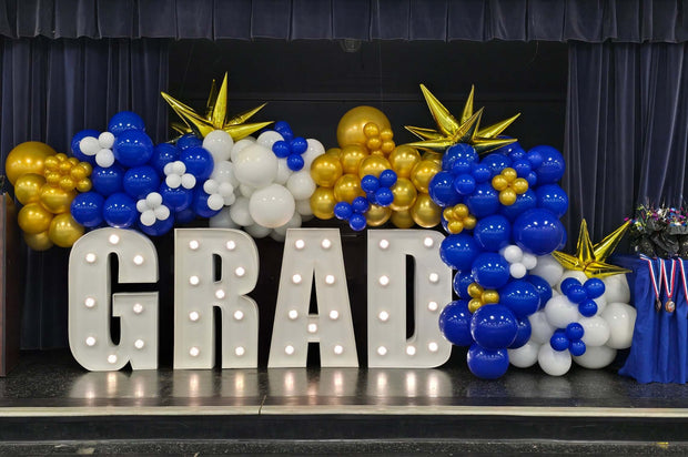 Graduation-themed balloon display with 'GRAD' letters on a stage.