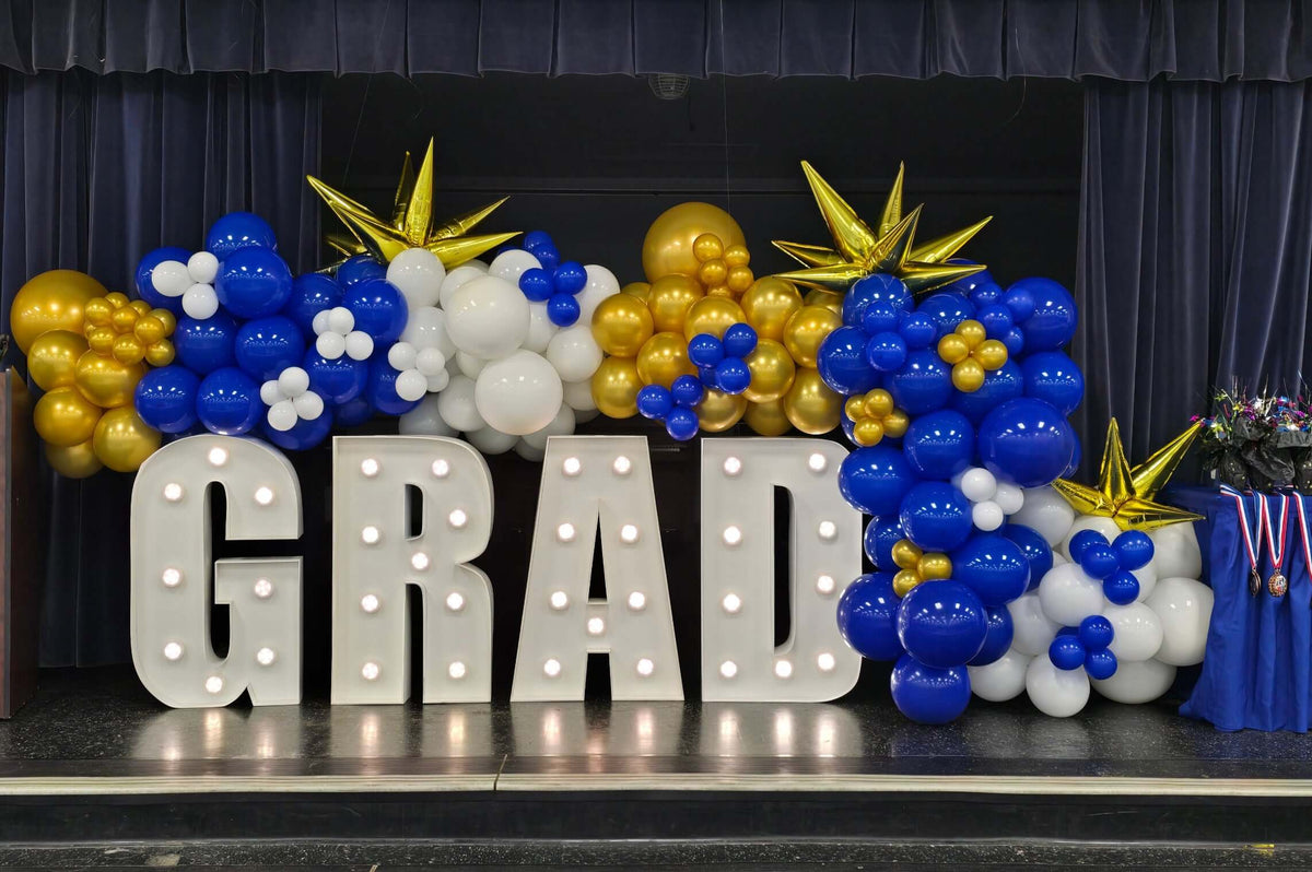 Graduation-themed balloon display with 'GRAD' letters on a stage.