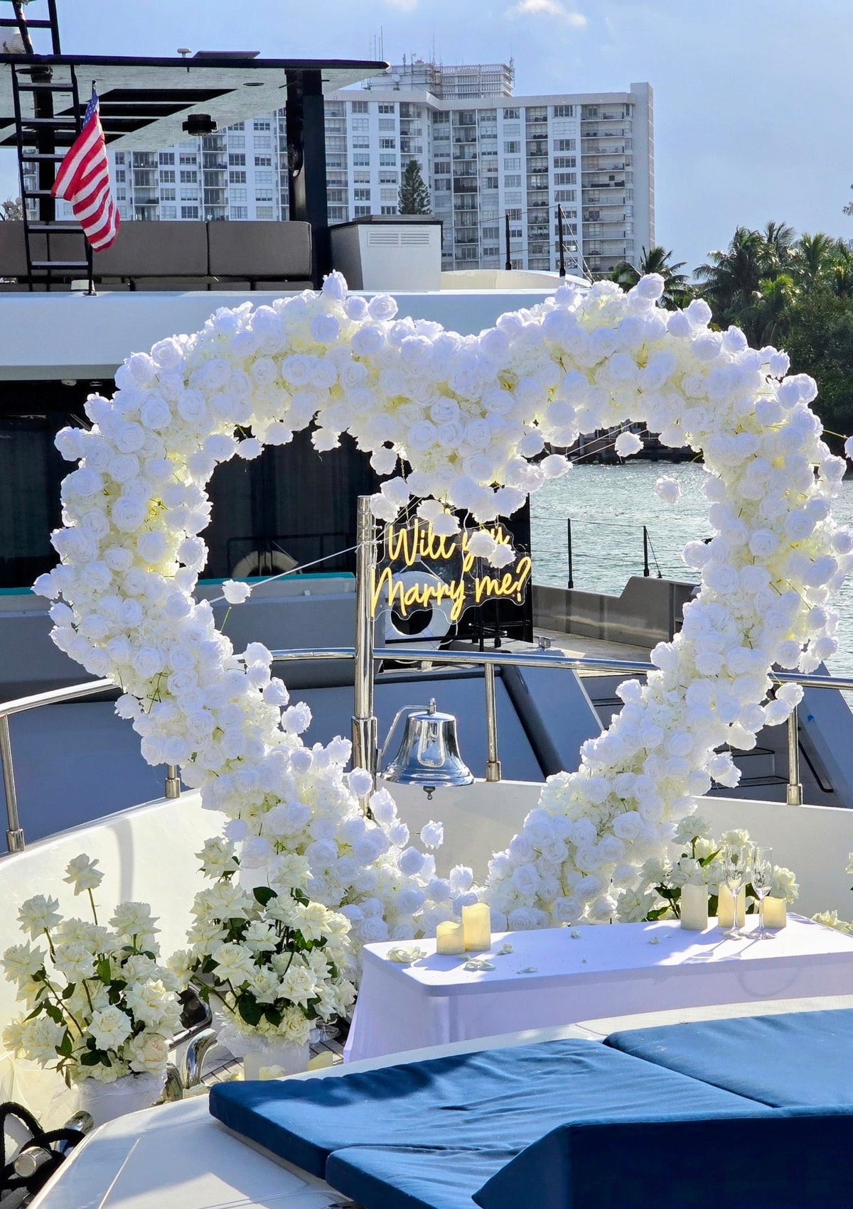 A stunning marriage proposal scene featuring a heart arch adorned with white flowers, creating a romantic backdrop on a boat.