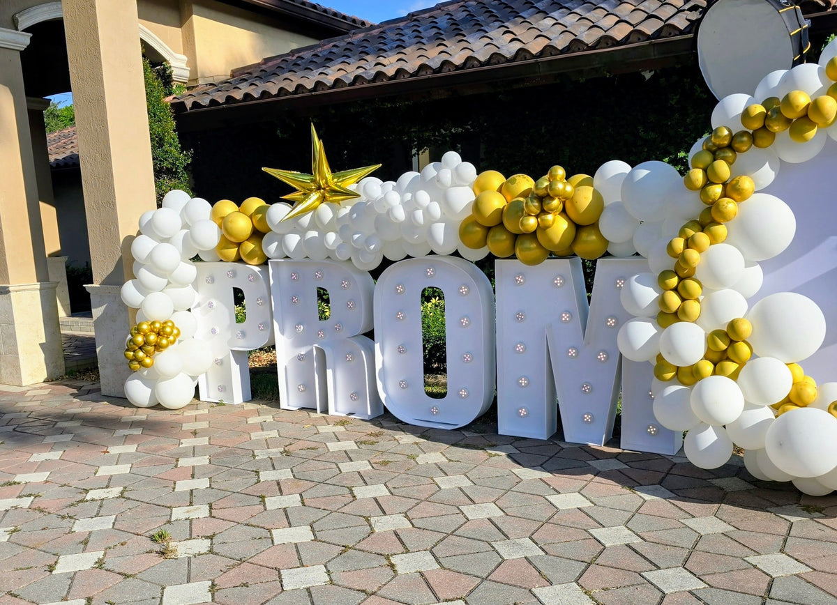 Decorative setup with 'PROM' letters surrounded by balloons on a stone patio.