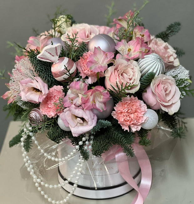 A floral Christmas Flower Box arrangement featuring pink and white flowers, greenery, and holiday decorations including a pearl necklace and a silver tray.