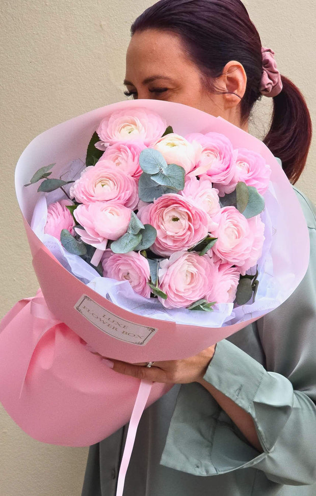 Ranunculus bouquet with eucalyptus, featuring pink ranunculus flowers in elegant packaging held by a woman.