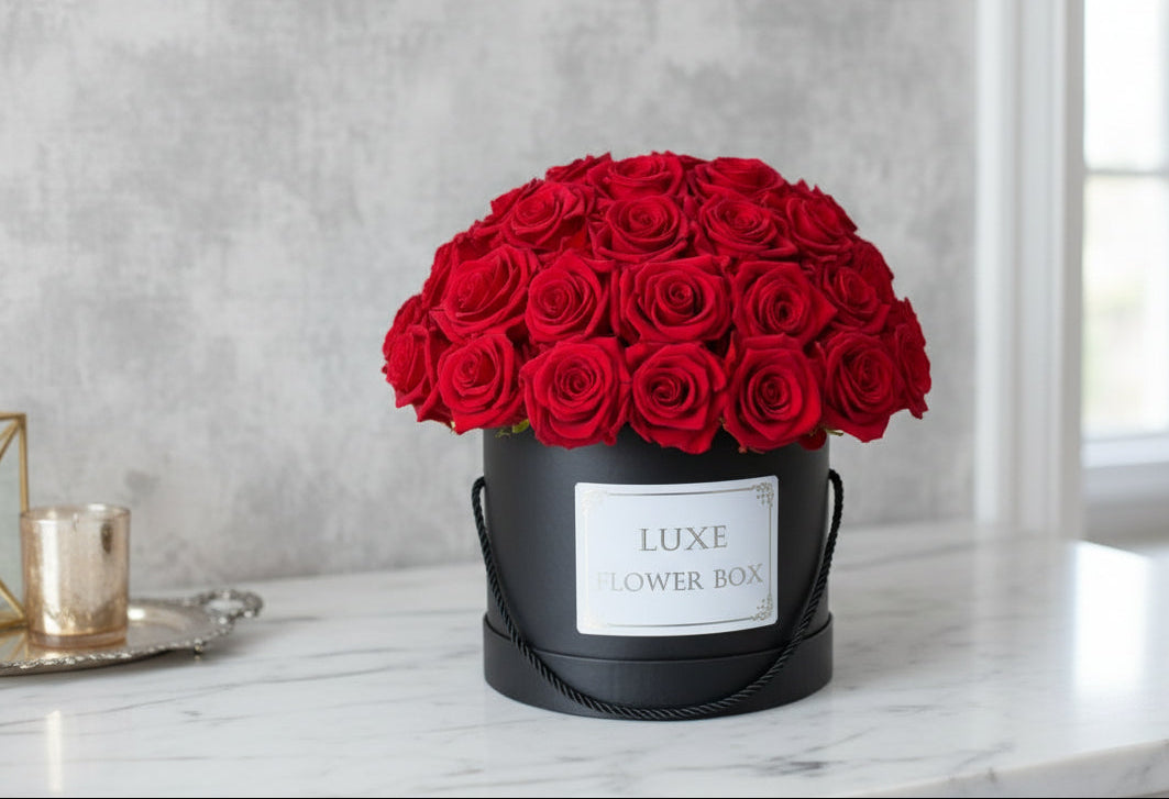 A round, black box with a preserve of red roses arranged neatly inside, labeled 'LUXE FLOWER BOX' on the front.