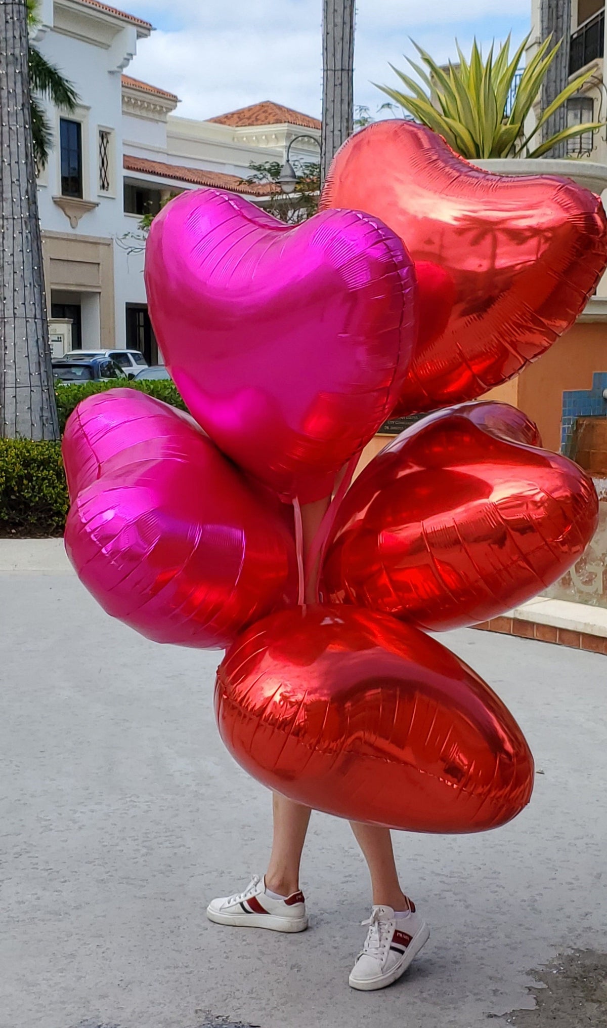 Person holding large red and pink heart-shaped balloons outdoors.