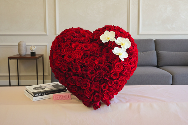 Heart-shaped arrangement of red roses with white orchids on a table in a living room setting.